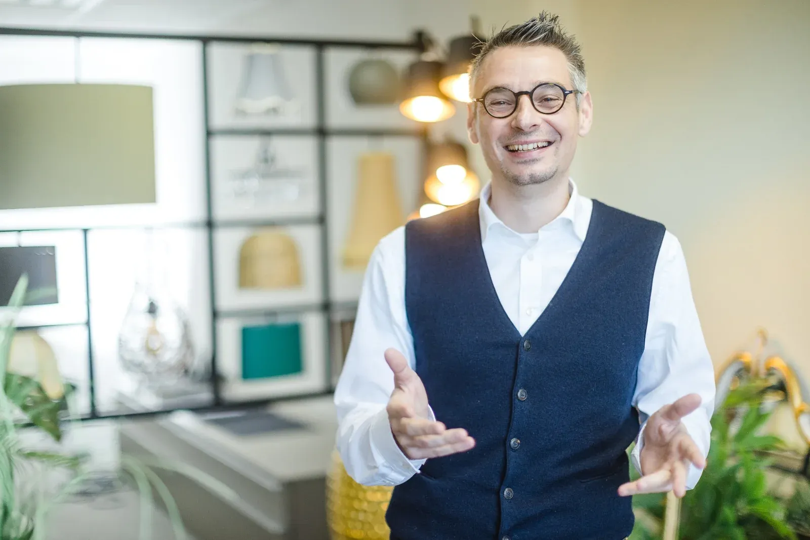 Patrick in Weste lächelt und breitet einladend die Hände aus