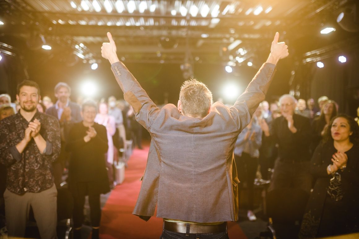 Patrick reckt beide Daumen in die Höhe, vor ihm steht und applaudiert das Publikum