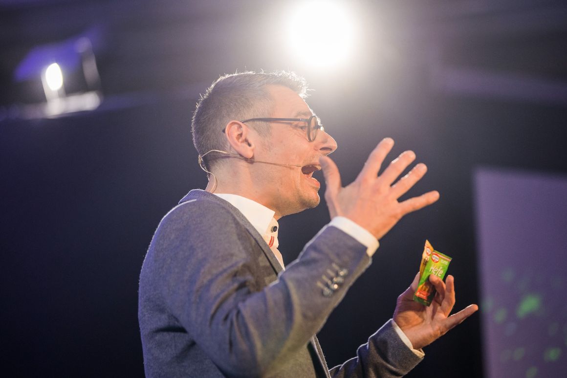 Patrick erklärt auf der Bühne mit lebhafter Geste, in der Hand ein Päckchen Hefe